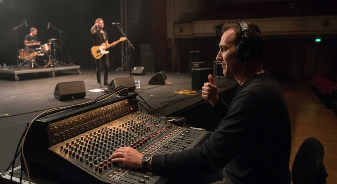 A Live Band on Stage with Monitor Wedges as a Sound Engineer Works a Mixing Console